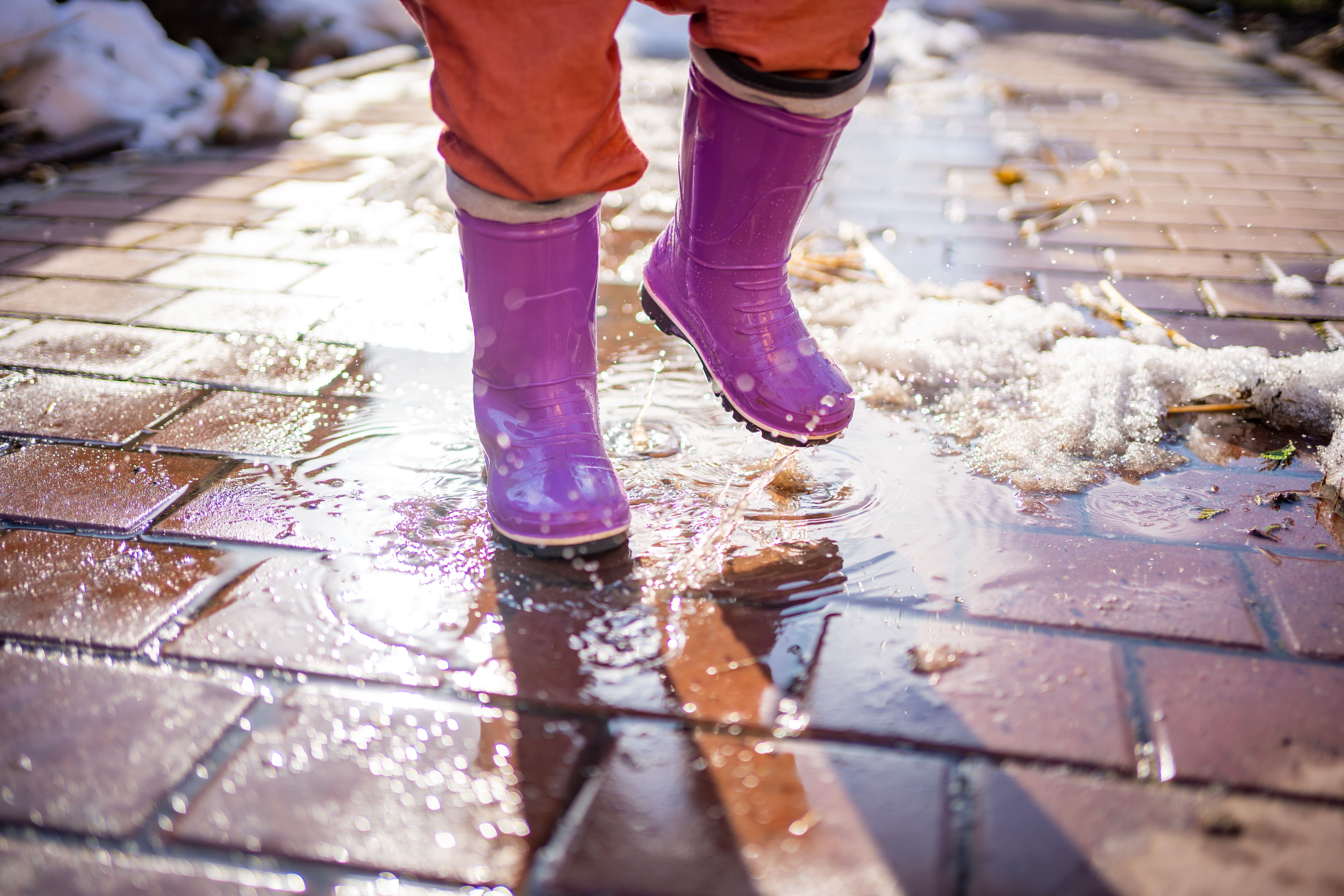 Child leaping puddles in rubber boots at sunset